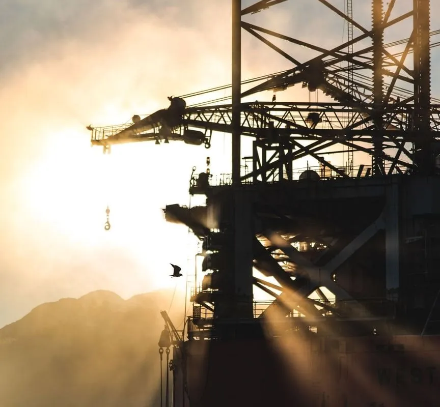 A gantry crane over a platform, silhouetted against a low sun
