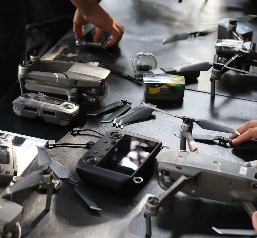 Hands at work over drones and their controllers, laid out across a bench